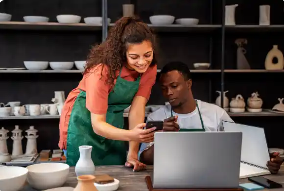 imagem mostra empreendedores trabalhando junto no computador um homem sentando e a mulher de pé ao lado dele.