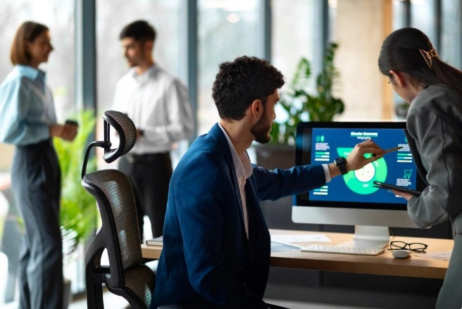 duas pessoas checando um gráfico no computador e duas ao fundo em um escritório, ilustrando a AI no mercado de trabalho.
